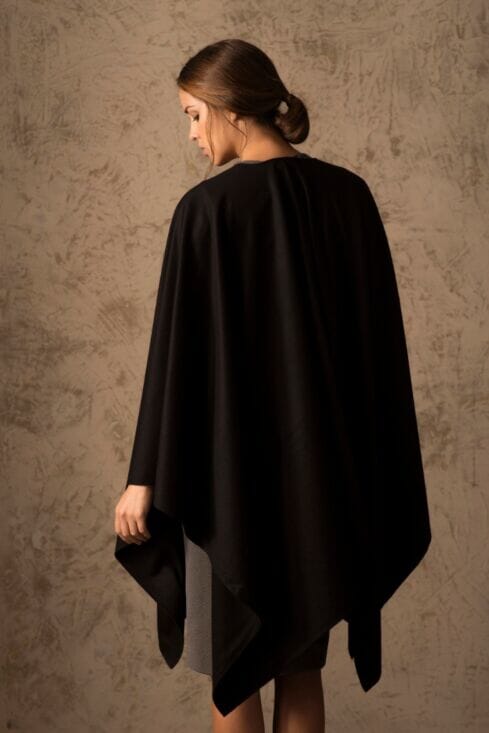 Woman wearing a black poncho against a textured brown wall