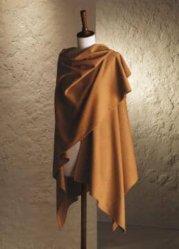 Brown shawl draped over a mannequin against a textured wall.
