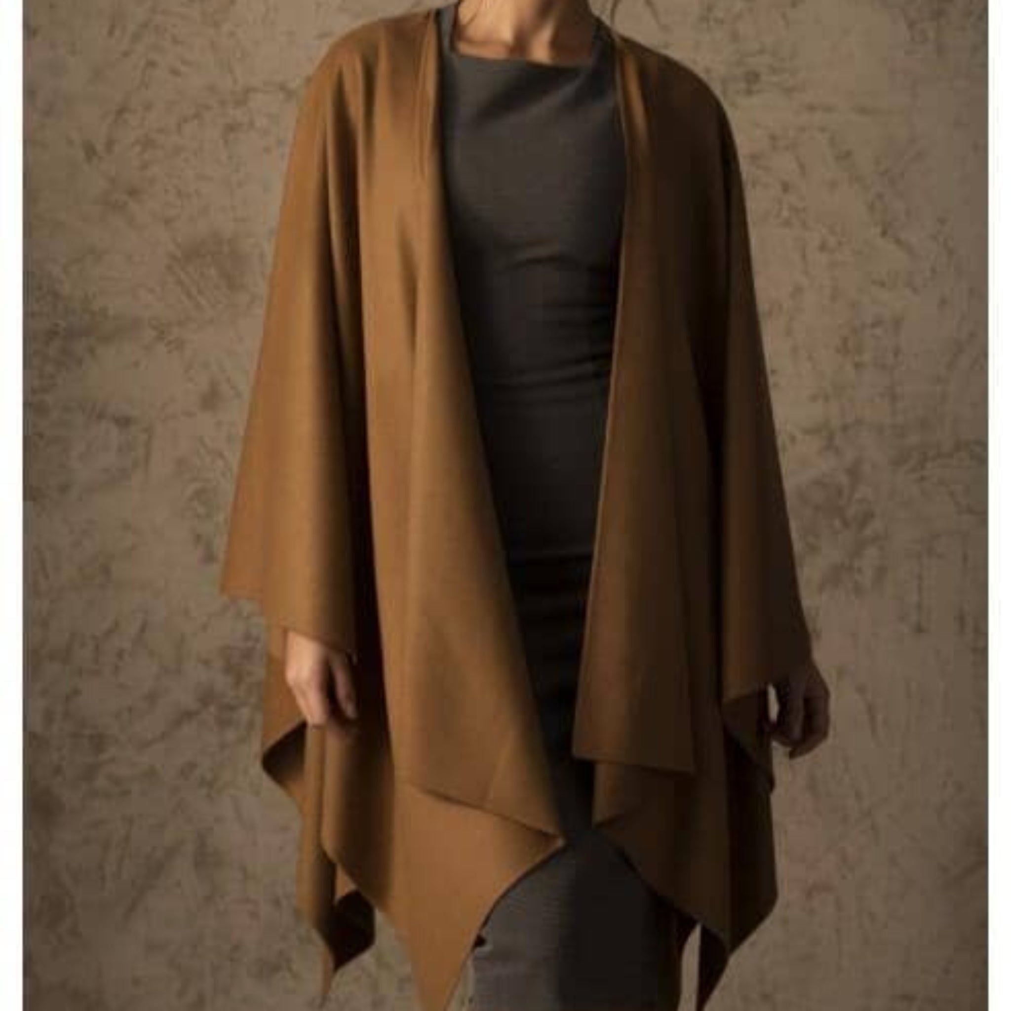 Woman wearing a brown draped garment against a textured wall.