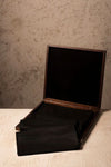 Open wooden box with black interior against a textured wall.