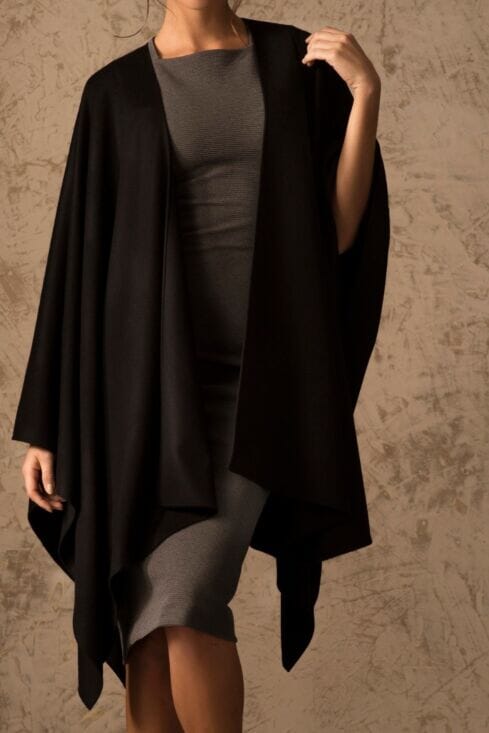 Person wearing a black coat over a gray dress against a textured beige background