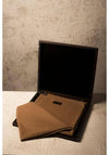 Brown folded fabric inside an open black suitcase against a textured wall.