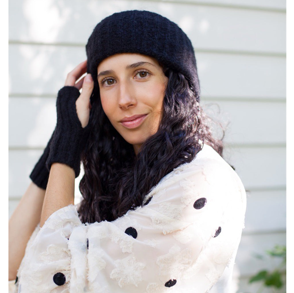 Woman wearing a black knit hat and gloves with a white coat featuring black buttons.