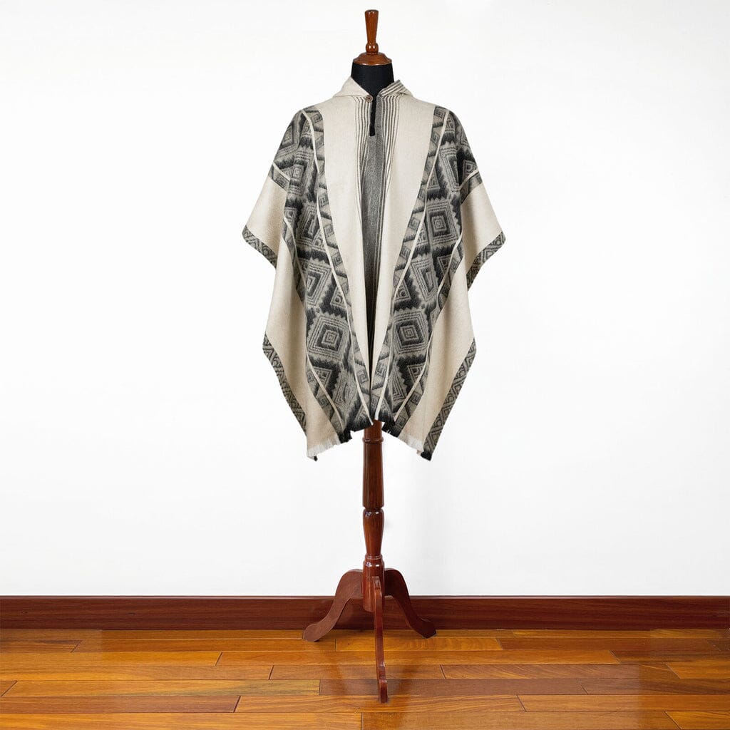 Mannequin wearing a patterned poncho on a wooden stand against a white wall.