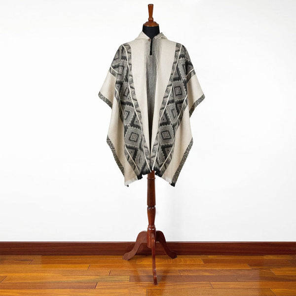 Mannequin wearing a patterned poncho on a wooden stand against a white wall.