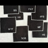 Set of eight black linen sweary cocktail coasters with white letter monogram design, laid flat on a surface