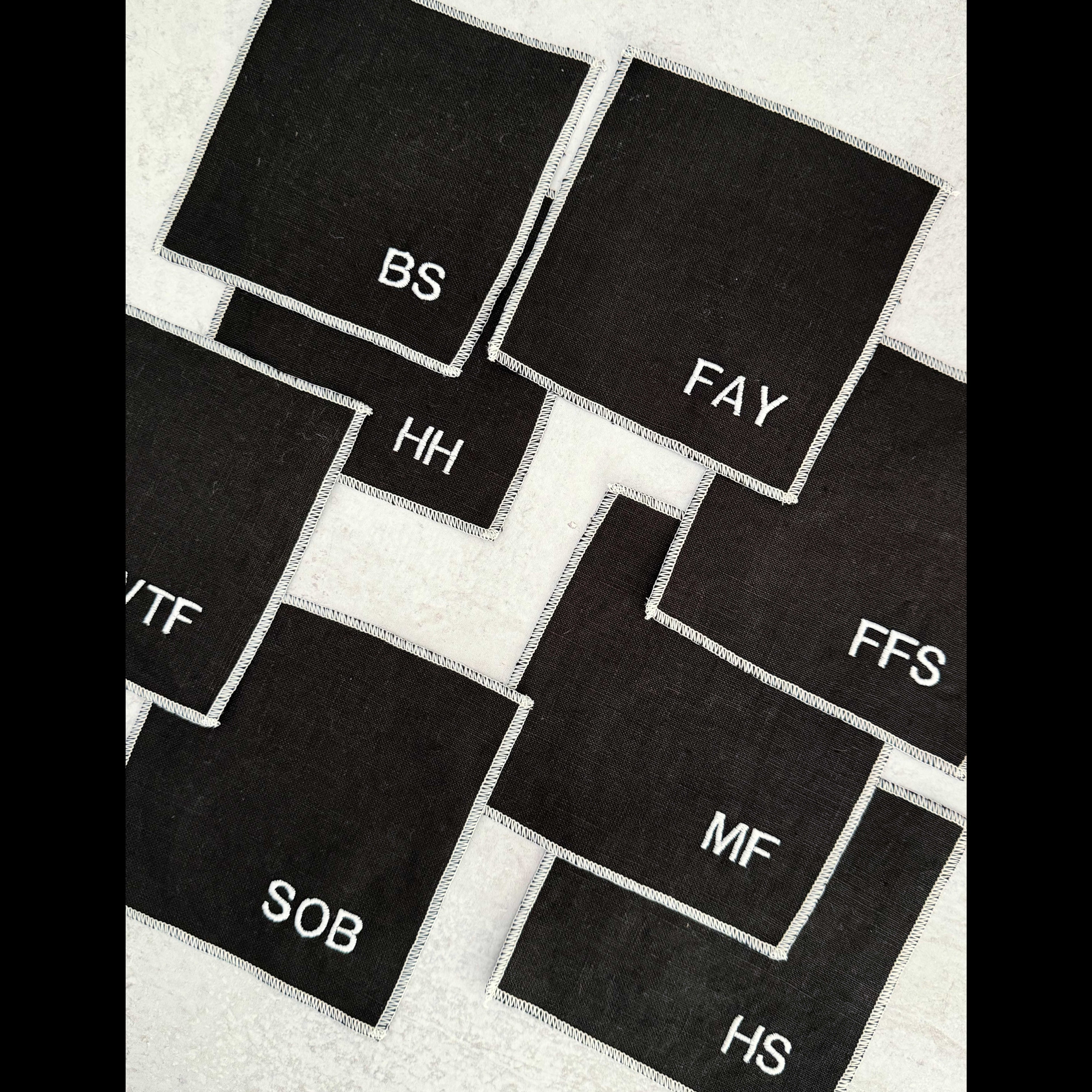 Close-up of black linen sweary coaster showing bold white lettering representing swear word monograms for a cocktail bar