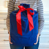 Person holding a large blue gift bag with a red ribbon