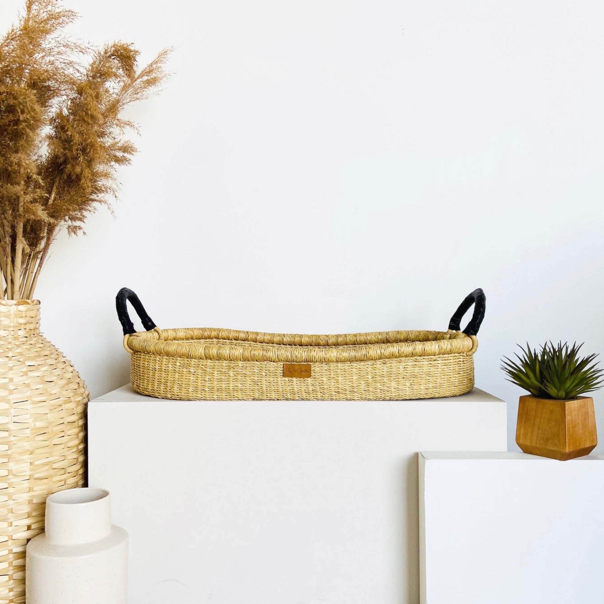 Wicker basket with handles on a white surface, surrounded by decorative items.
