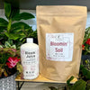 Bloomin' Soil package and Bloom Juice bottle with plants in the background. Bloom Power Bundle — fast-acting Bloom Juice with 150+ microbes & slow-release Bloomin' Soil for explosive flowering. More blooms, bigger color. Perfect garden gift.