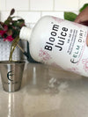 Bottle of 'Bloom Juice' being poured into a metal cup on a kitchen counter. Bloom Power Bundle — fast-acting Bloom Juice with 150+ microbes & slow-release Bloomin' Soil for explosive flowering. More blooms, bigger color. Perfect garden gift.
