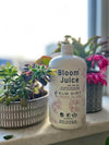 Bottle of 'Bloom Juice' on a windowsill with plants in the background. Bloom Power Bundle — fast-acting Bloom Juice with 150+ microbes & slow-release Bloomin' Soil for explosive flowering. More blooms, bigger color. Perfect garden gift.