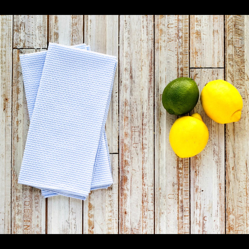 Blue seersucker cloth dinner napkins styled with lemons and limes on a wooden table