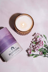 Candle in a glass holder with a purple container labeled 'Bluecorn Aromatica' on a light pink background.