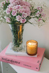 Vase with pink flowers and a lit candle on a pink book titled 'Catwalk' by Yves Saint Laurent.