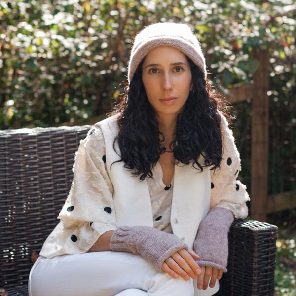Woman sitting outdoors wearing a white jacket with black polka dots and a pink beanie.