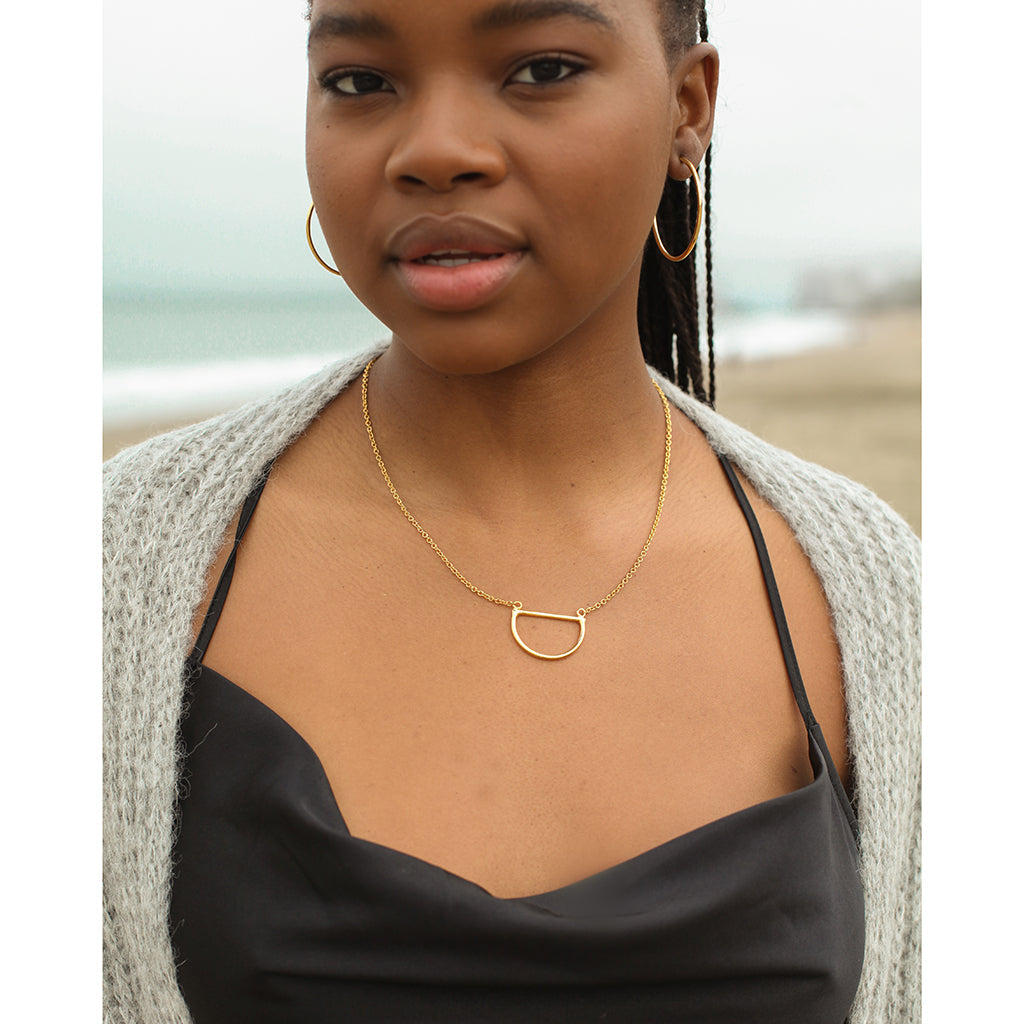 Woman wearing a gold necklace with a beach in the background