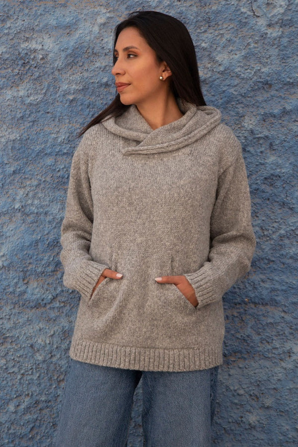 Woman wearing a gray sweater against a textured blue wall