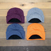 Four beanies in purple, gray, blue, and orange on a wooden surface.
