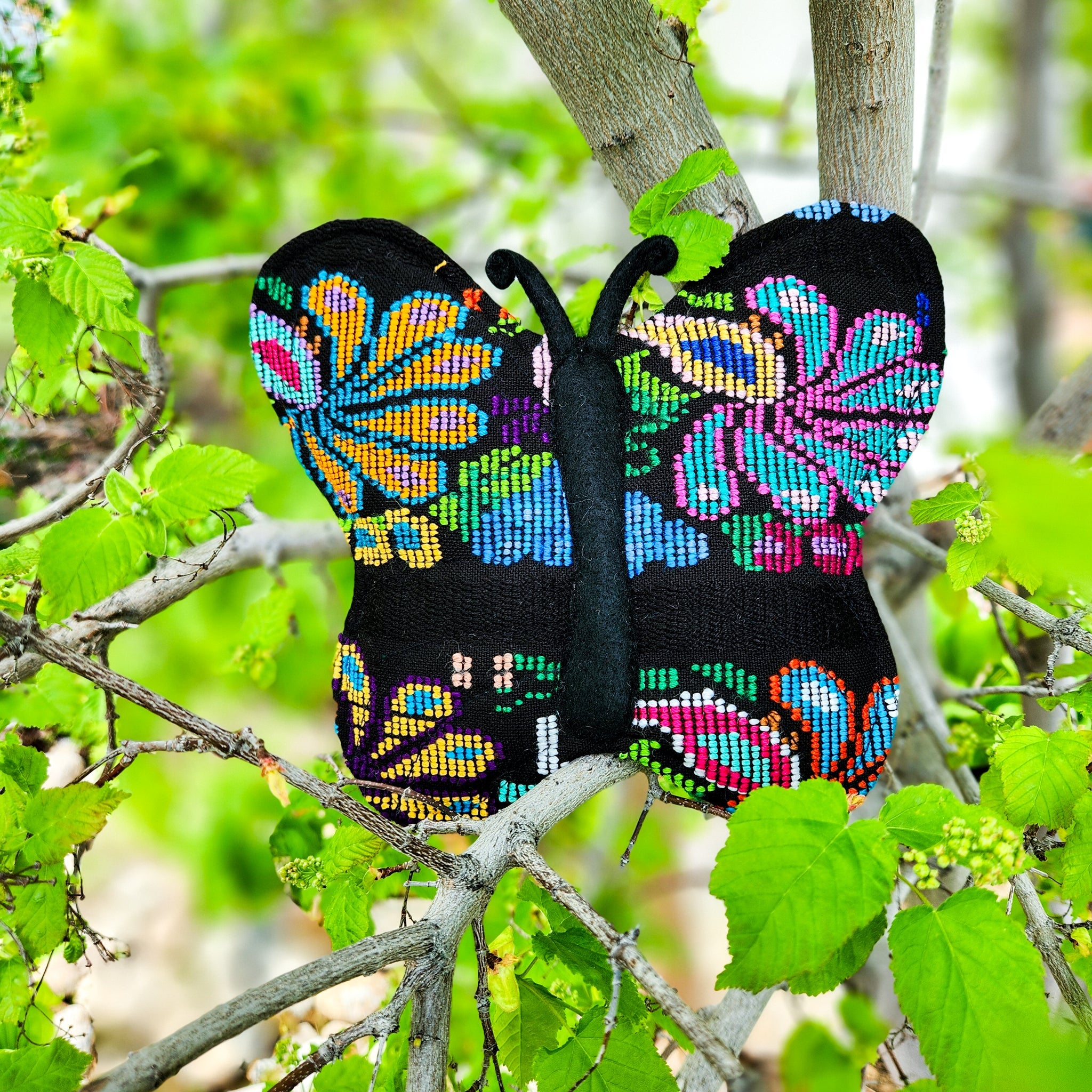 Colorful butterfly-shaped object on a branch with green leaves