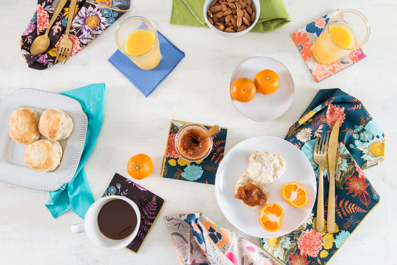 Brunch table styled with floral cloth napkins and cocktail napkins alongside biscuits, tangerines and juice