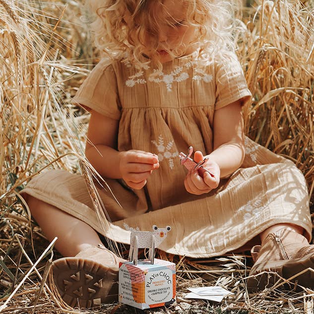 Child in a beige dress sitting in a field of wheat with a box of tissues.