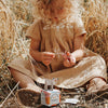 Child in a beige dress sitting in a field of wheat with a box of tissues.