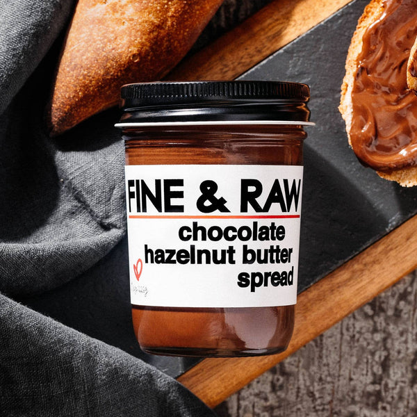 Jar of Fine & Raw chocolate hazelnut butter spread with bread on a wooden board.