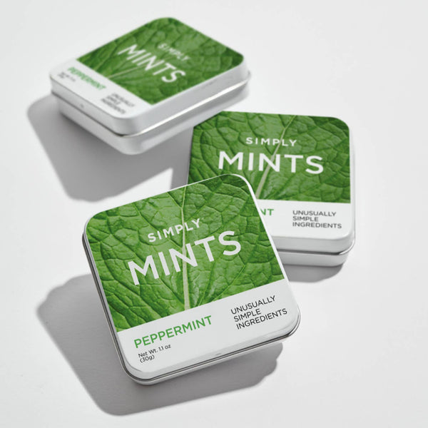 Three tins of 'Simply Mints' on a light gray background. Get instant freshness with SIMPLY MINTS - PEPPERMINT. Made with just three simple ingredients, including peppermint oil and cane sugar, for a clean and natural breath freshener.
