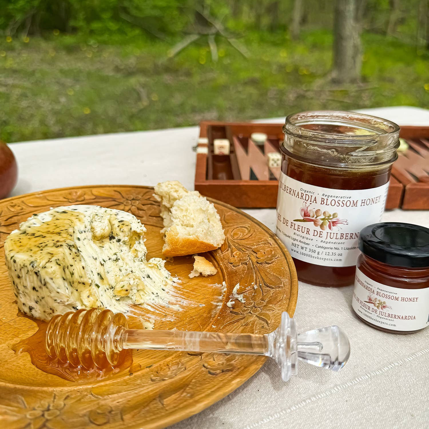 Butter with honey on a wooden plate with jars of honey in the background.