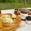 Butter with honey on a wooden plate with jars of honey in the background.