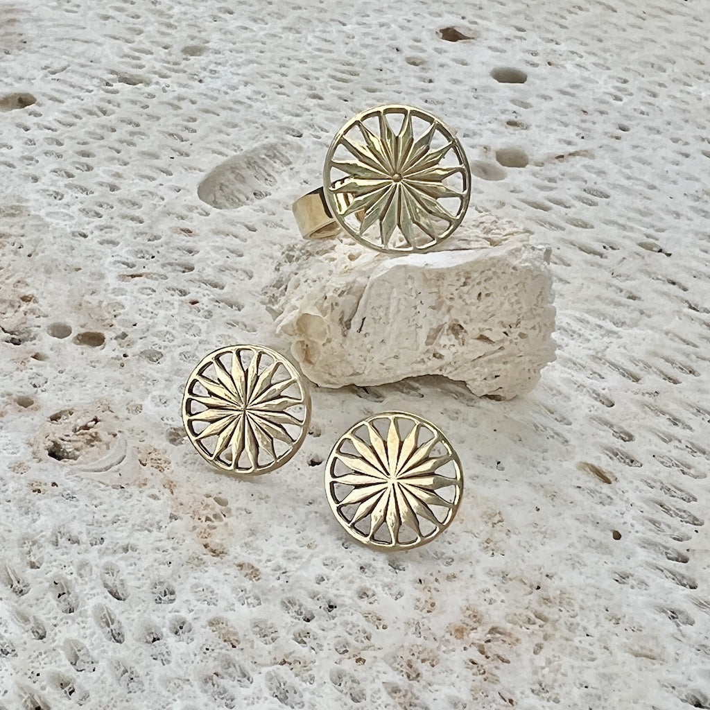 Gold sunburst ring and earrings on a textured stone surface