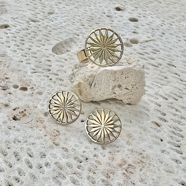 Gold sunburst ring and earrings on a textured stone surface