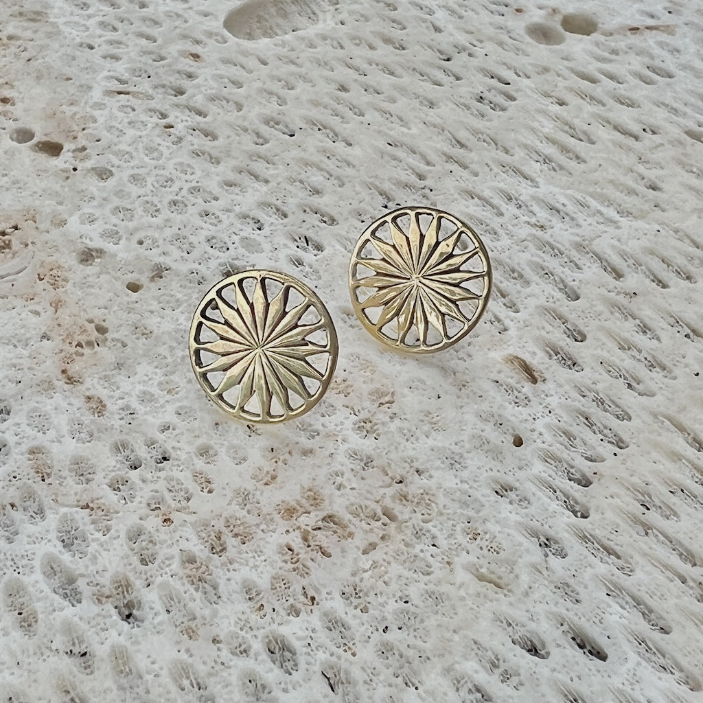Gold sunburst patterned earrings on a textured stone surface