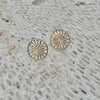 Gold sunburst patterned earrings on a textured stone surface