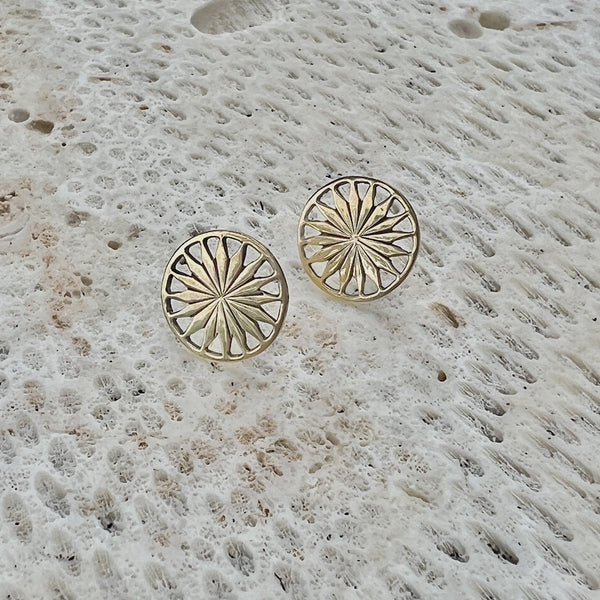Gold sunburst patterned earrings on a textured stone surface