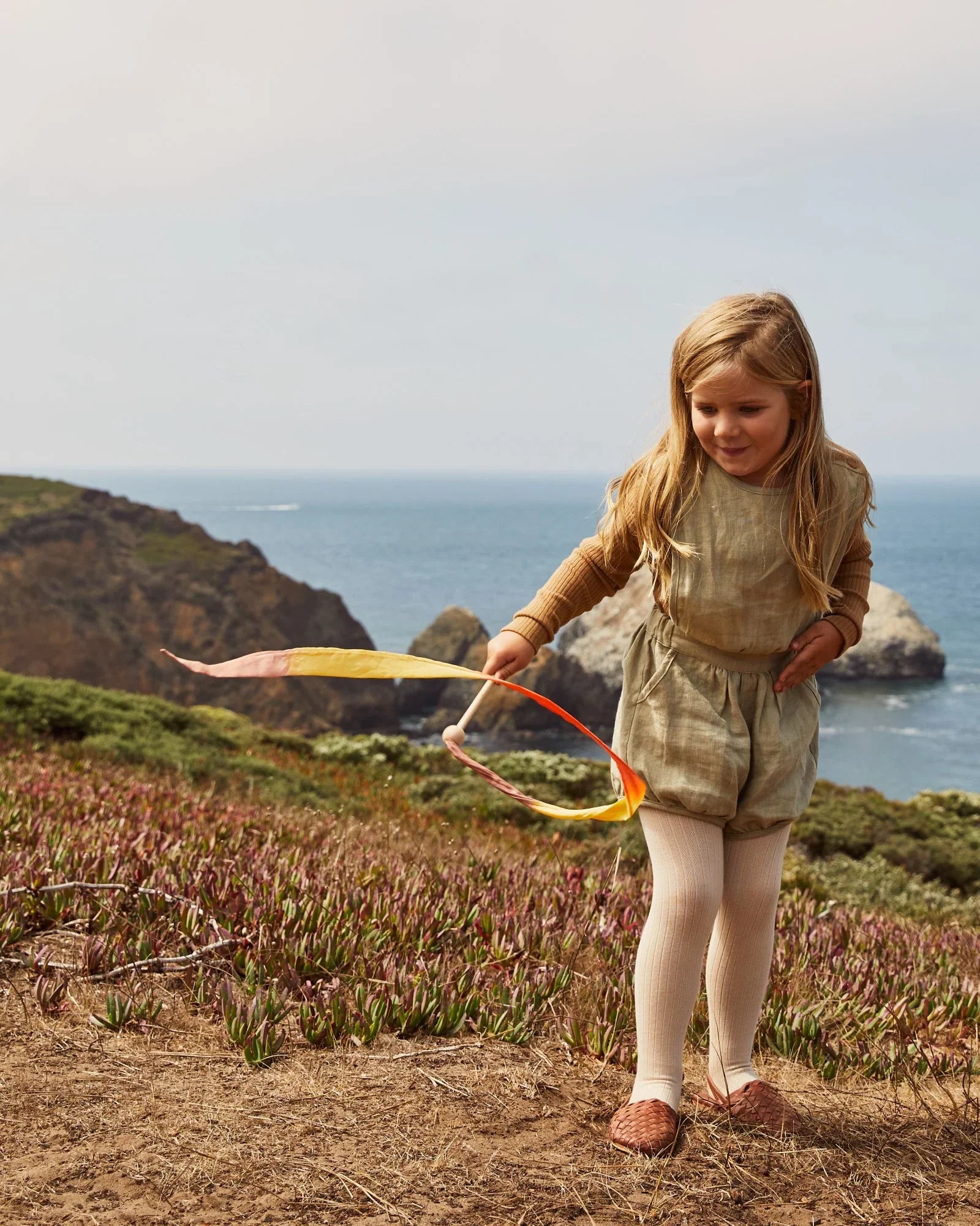 Young girl playing with a ribbon on a coastal cliffside