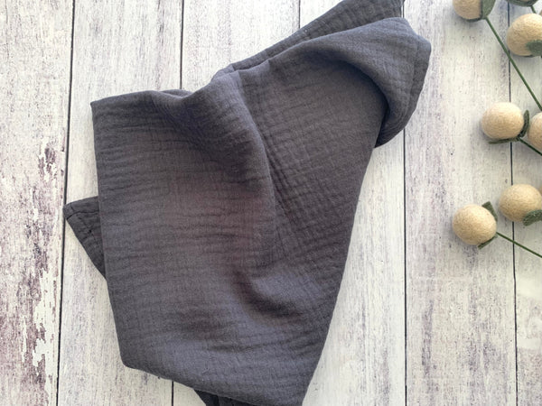 Dark gray textured fabric on a light wooden surface with small round objects and green stems.
