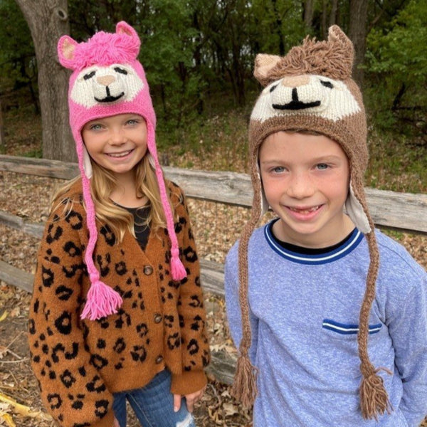 Two children wearing animal-themed hats outdoors with trees in the background