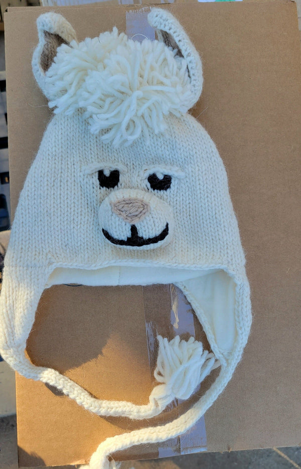 White knitted hat with llama face design on a cardboard background