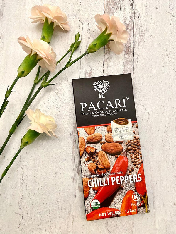 Pacari chocolate bar with chilli peppers on a light gray surface with flowers.