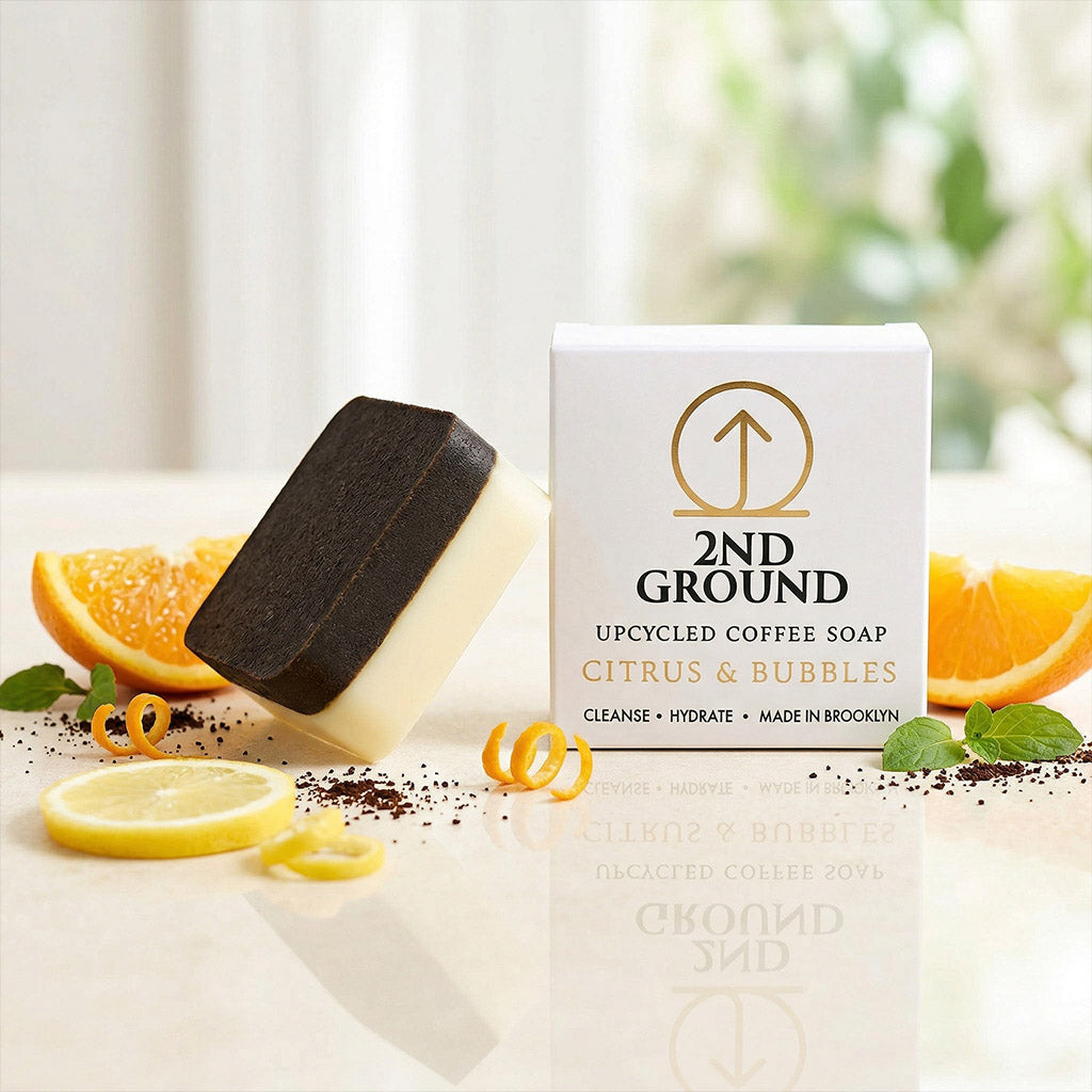 Upcycled coffee soap with packaging on a light surface with citrus fruits and coffee grounds.