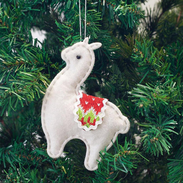 White llama ornament with red and green pattern hanging on a Christmas tree.