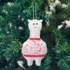 White llama ornament with a colorful skirt hanging on a Christmas tree.