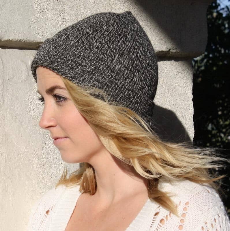 Woman wearing a gray knit beanie against a light-colored wall.