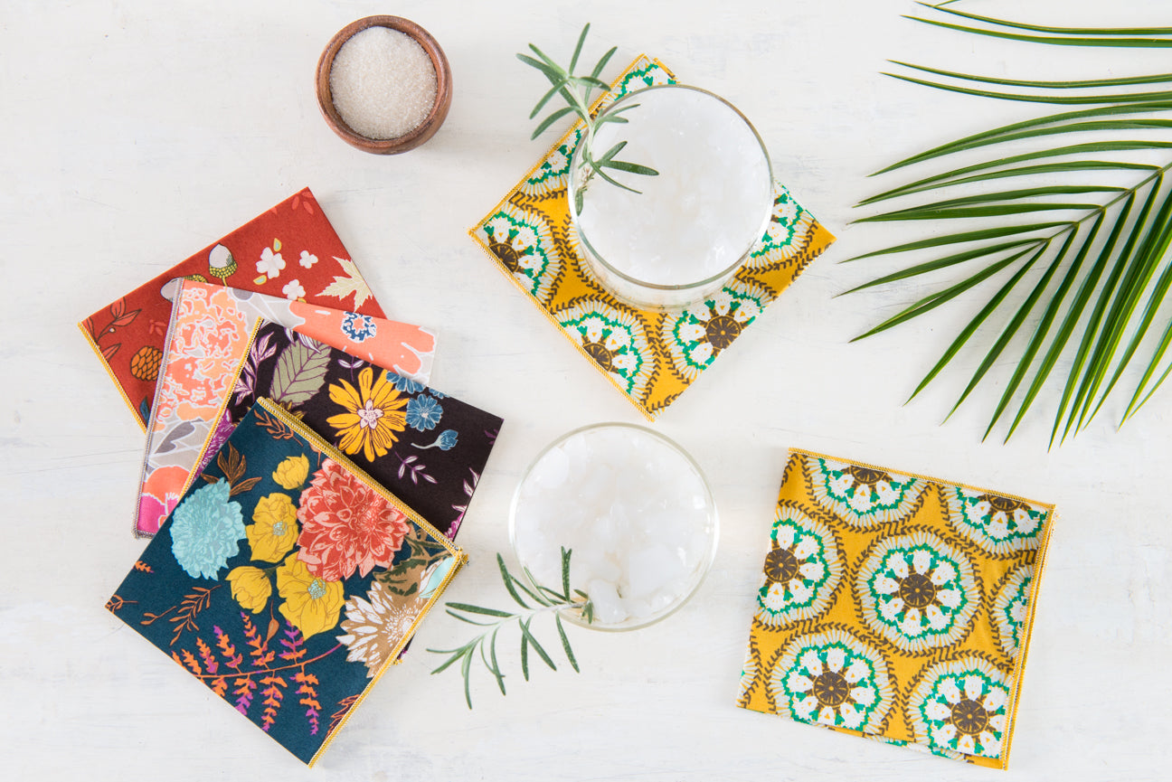 Floral cocktail napkins displayed with a rosemary cocktail, palm frond and salt cellar on a table