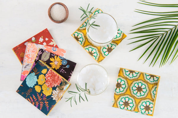 Floral cocktail napkins displayed with a rosemary cocktail, palm frond and salt cellar on a table