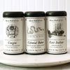 A high-quality photograph of the Colonial Black Tea Trio, showcasing the three signature tea tins and a steaming cup of tea.