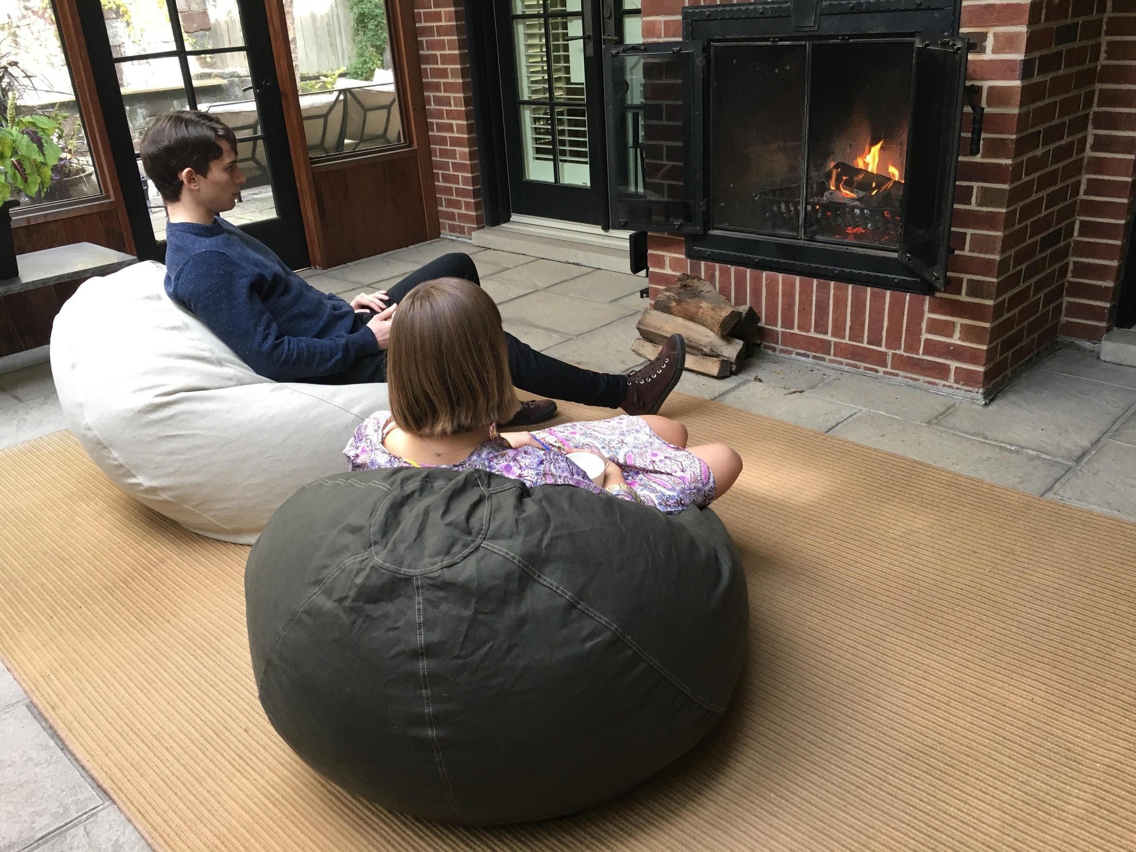 Two people sitting on bean bags in front of a fireplace.