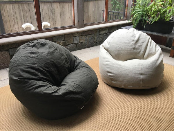 Two bean bags, one black and one white, on a wooden floor with a window and plant in the background.